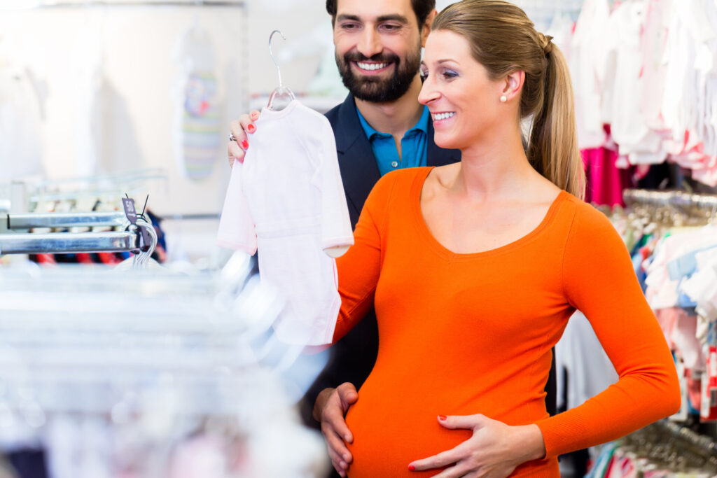 Schwangere Frau und Mann kaufen Babykleidung im Geschäft