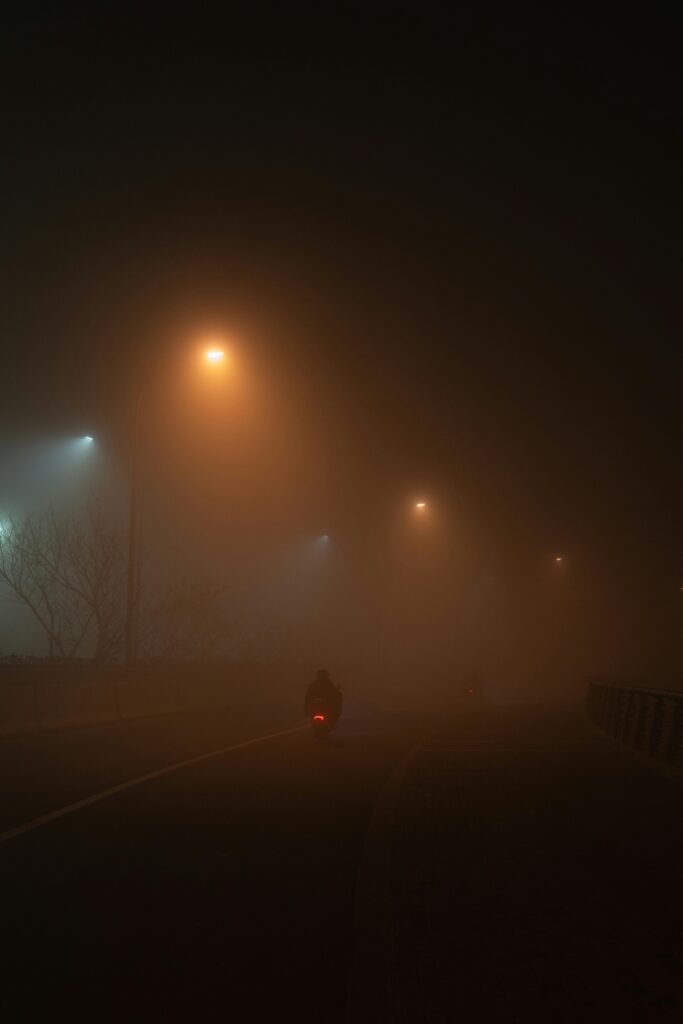 Ein Motorradfahrer auf einem Motorrad bis 500 ccm fährt auf einer von Straßenlaternen beleuchteten Straße, umgeben von dichtem Nebel, der eine geheimnisvolle Atmosphäre schafft