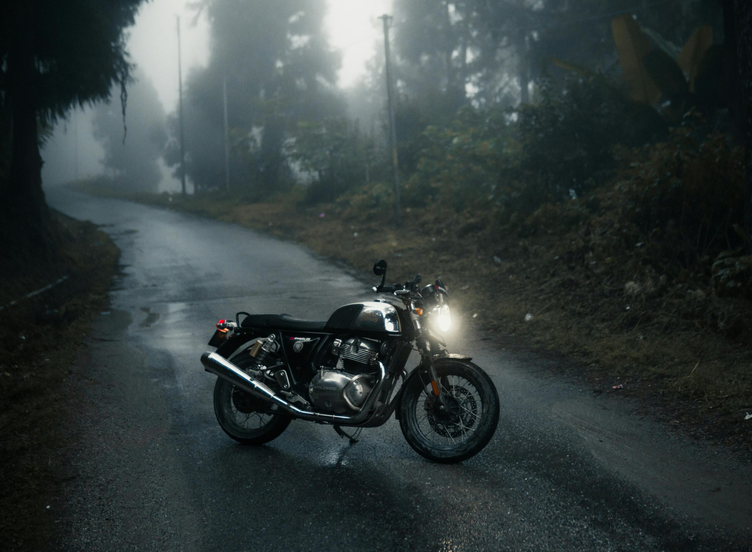 Ein Motorrad bis 500 ccm geparkt auf einer nebligen Straße, umgeben von einer mystischen Waldlandschaft, beleuchtet die Szene mit seinem Scheinwerfer und lädt zu einer stimmungsvollen Fahrt ein
