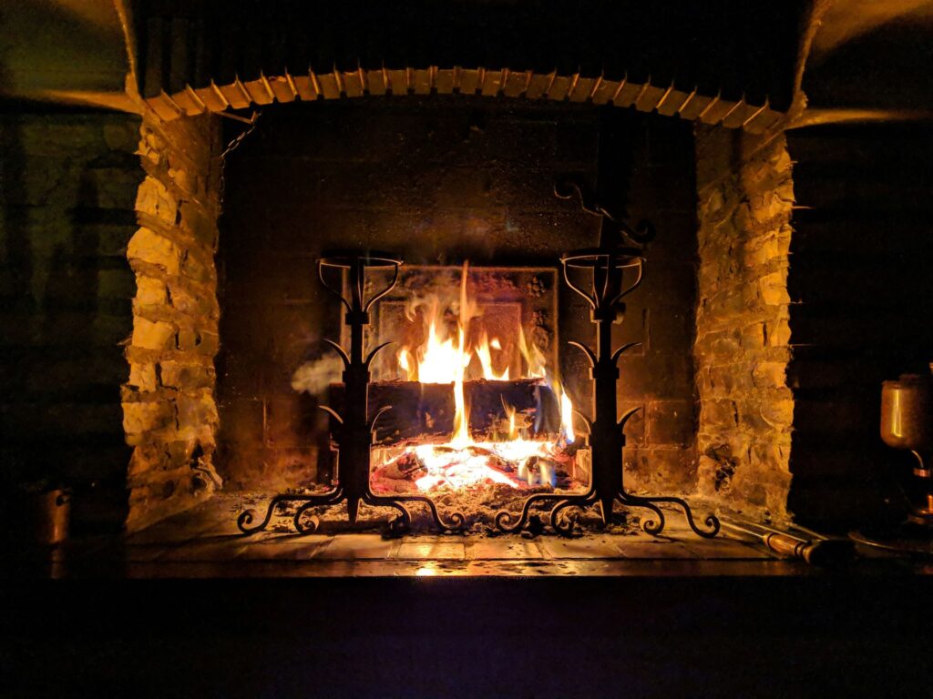 Rustikaler Kamin aus Stein mit brennendem Feuer, schmiedeeiserne Halterungen und glühende Holzscheite.