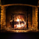 Rustikaler Kamin aus Stein mit brennendem Feuer, schmiedeeiserne Halterungen und glühende Holzscheite.