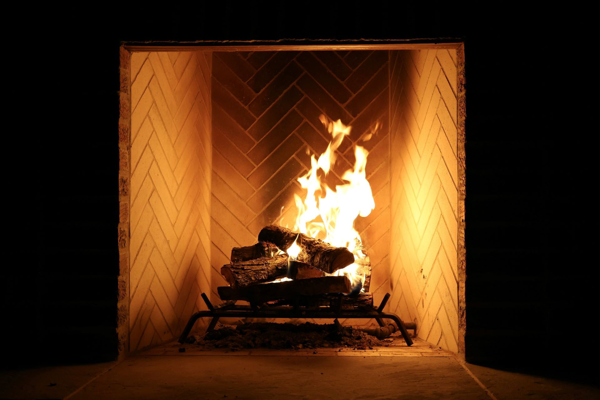 Heller Kamin mit brennenden Holzscheiten, modernes Fischgrätenmuster im Hintergrund.