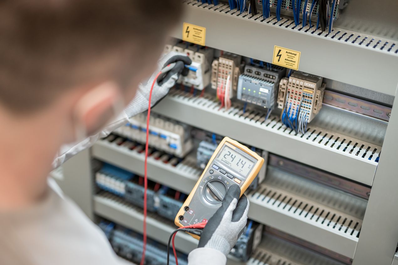 Elektroniker prueft Spannung an einem Hutschienen Switch im montierten Schaltschrank mit Multimeter